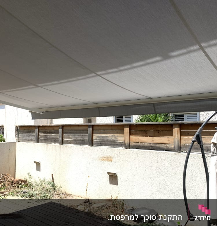 סוכך בד אפור מתוח מעל חצר מרוצפת עץ